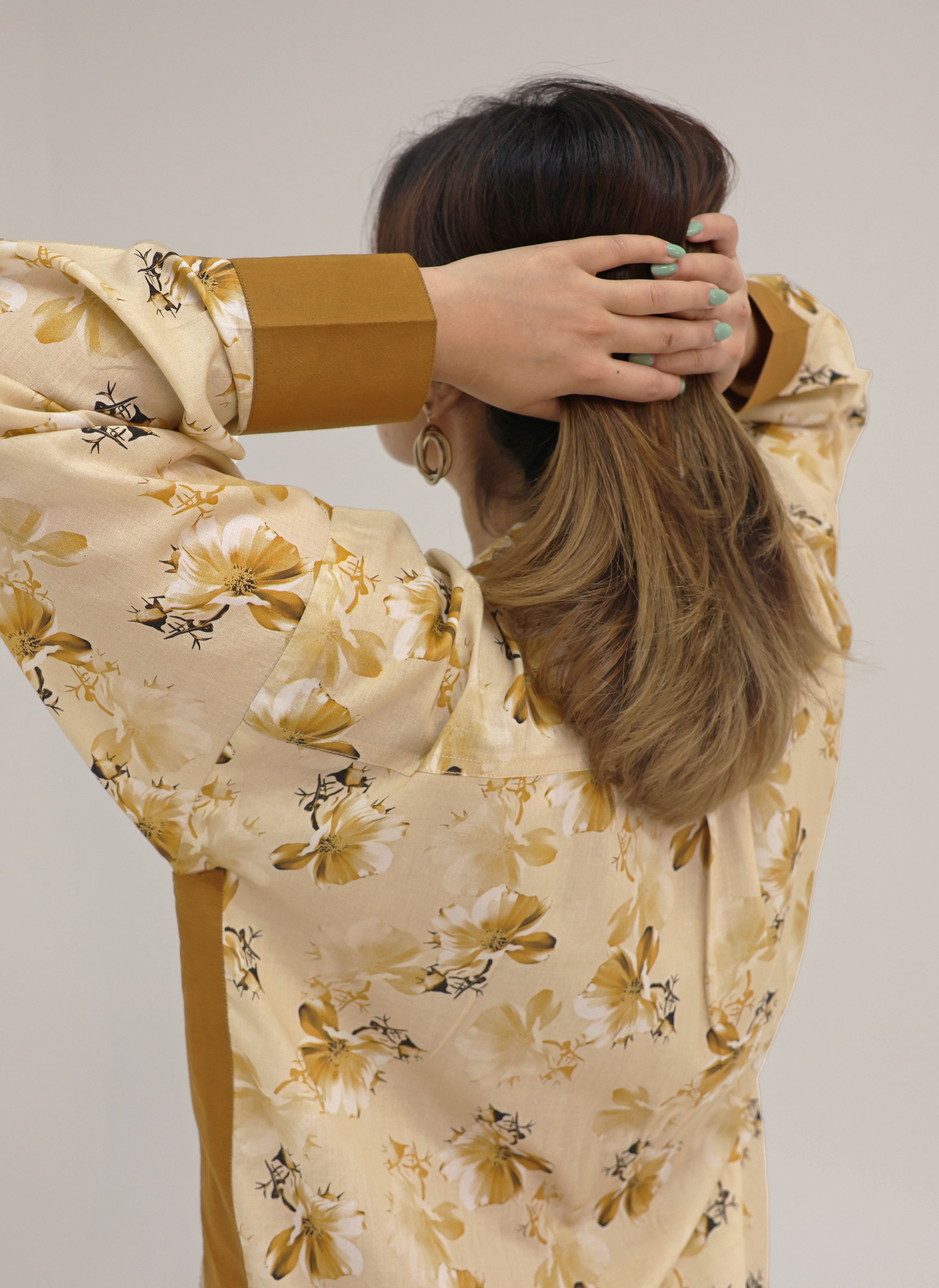Person wearing a beige floral dress with brown accents, holding their hair.